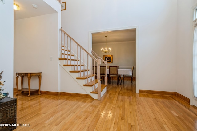 foyer featuring crown molding, wood-type flooring, stairway, an inviting chandelier, and baseboards