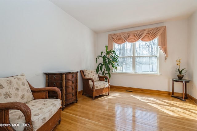 living area featuring lofted ceiling, light wood finished floors, visible vents, and baseboards