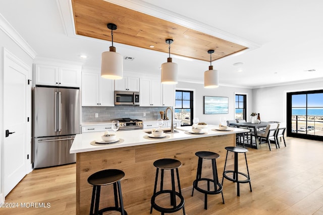 kitchen featuring decorative light fixtures, a kitchen island with sink, white cabinets, and appliances with stainless steel finishes