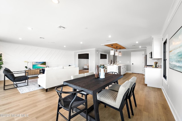 dining room with sink, light wood-type flooring, and ornamental molding