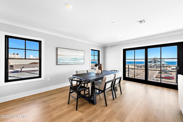 dining room featuring light wood-type flooring, ornamental molding, and a water view