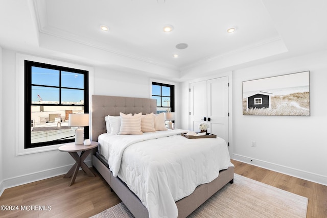 bedroom with crown molding, hardwood / wood-style floors, and a raised ceiling