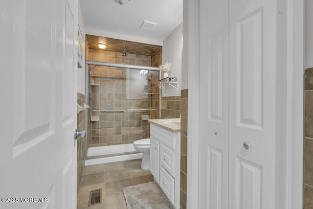 bathroom featuring a shower with shower door, toilet, vanity, and tile patterned flooring