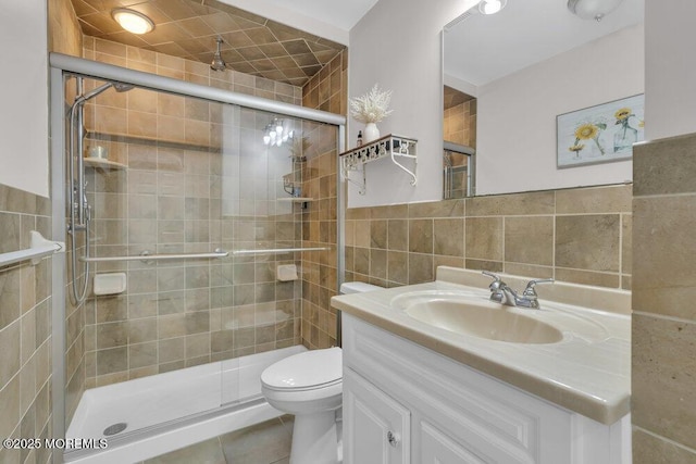 bathroom with toilet, vanity, tile walls, tile patterned flooring, and a shower with door