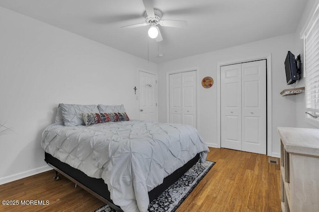 bedroom with ceiling fan, hardwood / wood-style flooring, and multiple closets