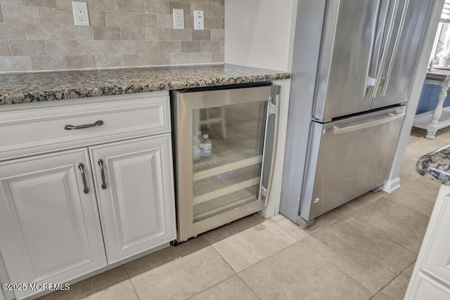 kitchen with light tile patterned floors, white cabinetry, dark stone countertops, beverage cooler, and stainless steel refrigerator