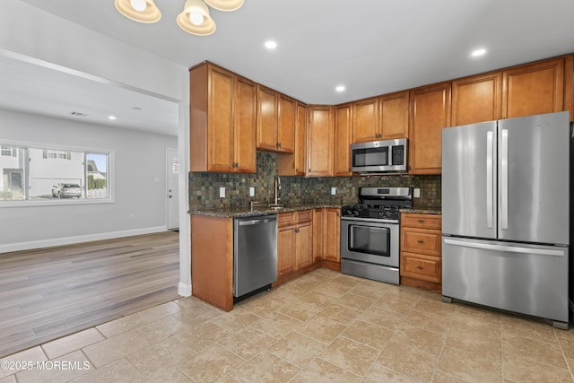 kitchen with appliances with stainless steel finishes, tasteful backsplash, light wood-type flooring, dark stone counters, and sink