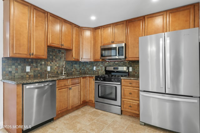 kitchen with sink, stainless steel appliances, dark stone counters, and tasteful backsplash