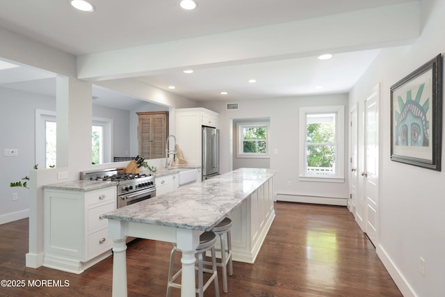 kitchen with a baseboard heating unit, a kitchen bar, white cabinetry, and premium appliances