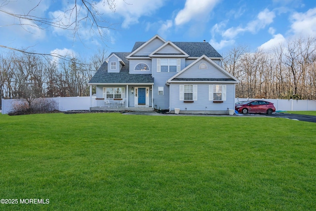 view of front of home featuring roof with shingles, fence, a porch, and a front yard