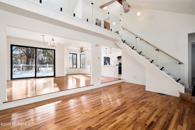 unfurnished living room featuring hardwood / wood-style floors, ceiling fan with notable chandelier, and high vaulted ceiling