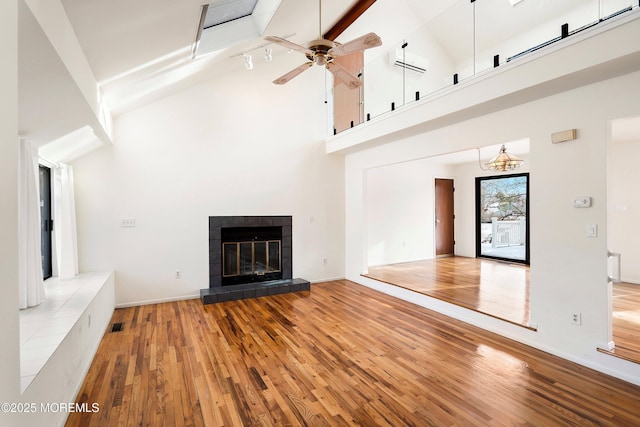 unfurnished living room with ceiling fan, hardwood / wood-style floors, high vaulted ceiling, a fireplace, and beamed ceiling