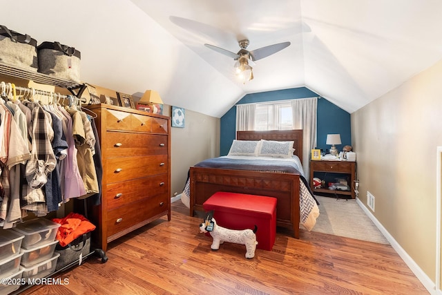 bedroom featuring ceiling fan, wood finished floors, visible vents, baseboards, and vaulted ceiling