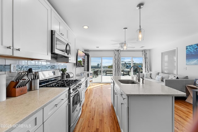 kitchen featuring stainless steel appliances, a kitchen island with sink, white cabinetry, ceiling fan, and sink