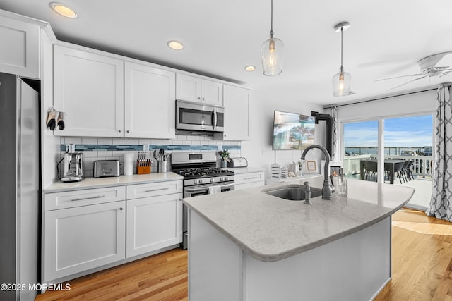 kitchen featuring stainless steel appliances, a center island with sink, decorative light fixtures, and white cabinetry