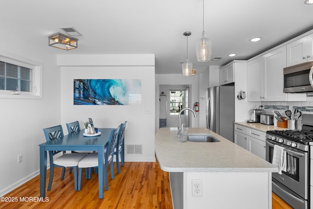 kitchen featuring a kitchen island with sink, stainless steel appliances, pendant lighting, sink, and tasteful backsplash