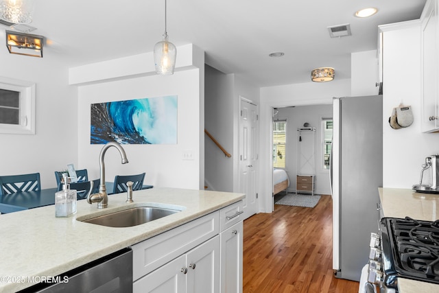 kitchen with pendant lighting, light hardwood / wood-style floors, white cabinetry, appliances with stainless steel finishes, and sink