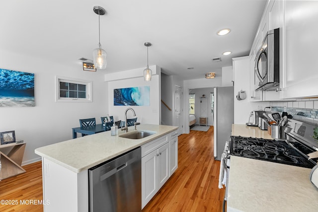 kitchen featuring pendant lighting, light wood-type flooring, white cabinetry, appliances with stainless steel finishes, and sink