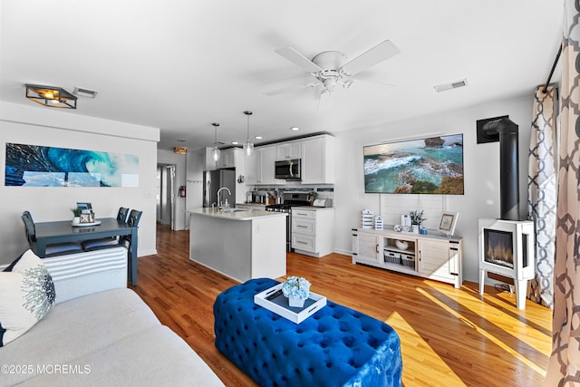 living room with ceiling fan, light hardwood / wood-style flooring, a wood stove, and sink