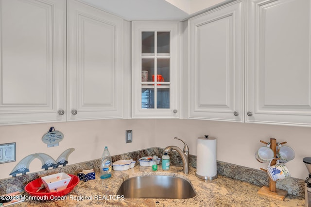 kitchen featuring white cabinets, light stone counters, and sink