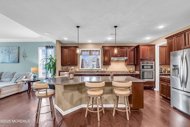 kitchen with a center island with sink, appliances with stainless steel finishes, a kitchen breakfast bar, hanging light fixtures, and light stone countertops