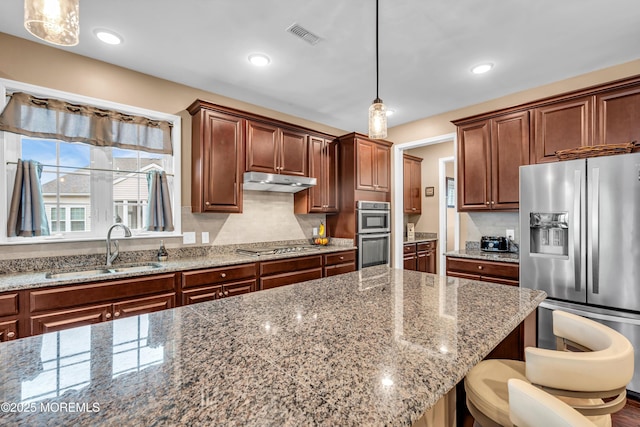 kitchen featuring appliances with stainless steel finishes, a kitchen bar, decorative light fixtures, sink, and light stone counters