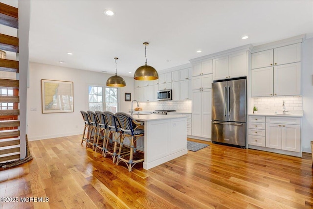 kitchen featuring decorative light fixtures, a center island with sink, tasteful backsplash, white cabinets, and appliances with stainless steel finishes