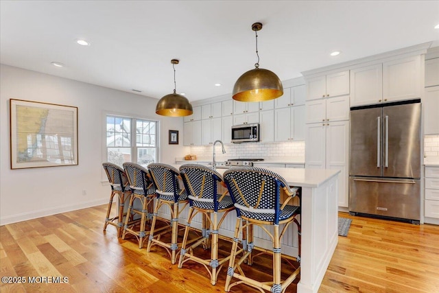 kitchen featuring white cabinets, stainless steel appliances, a center island with sink, and pendant lighting