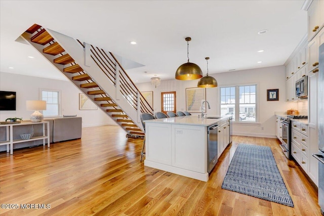 kitchen with sink, decorative light fixtures, white cabinetry, a kitchen island with sink, and appliances with stainless steel finishes