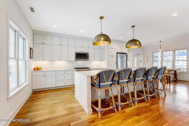 kitchen featuring appliances with stainless steel finishes, pendant lighting, white cabinets, and a kitchen island