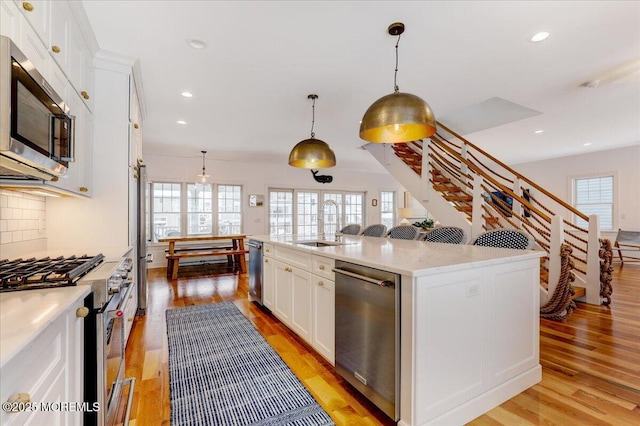 kitchen with stainless steel appliances, sink, white cabinets, an island with sink, and hanging light fixtures