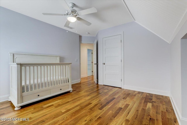 unfurnished bedroom featuring ceiling fan, hardwood / wood-style floors, lofted ceiling, and a nursery area