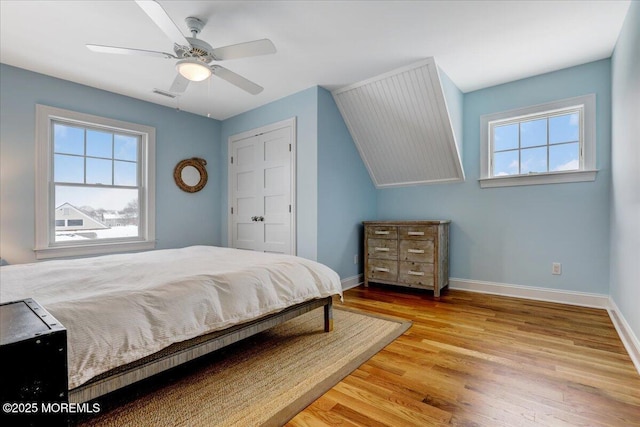 bedroom with light wood-type flooring, ceiling fan, a closet, and multiple windows