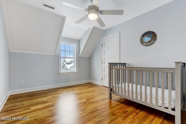 bedroom featuring a nursery area, ceiling fan, vaulted ceiling, and wood-type flooring