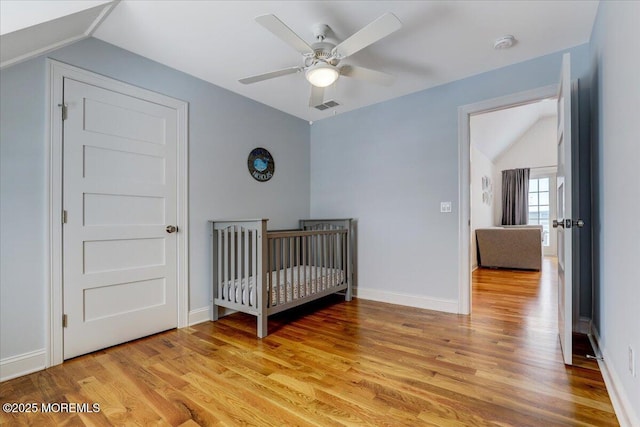 bedroom featuring lofted ceiling, ceiling fan, a crib, and light hardwood / wood-style flooring