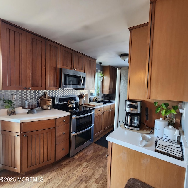 kitchen with appliances with stainless steel finishes, decorative light fixtures, tasteful backsplash, sink, and light wood-type flooring