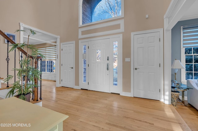 entrance foyer featuring baseboards, light wood-style flooring, and a towering ceiling