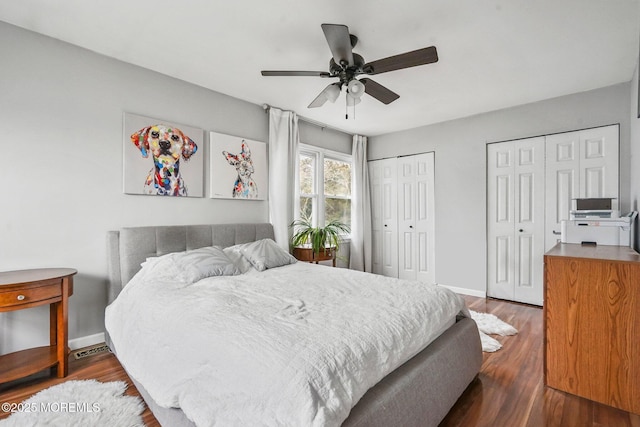 bedroom with ceiling fan, dark wood-type flooring, and multiple closets