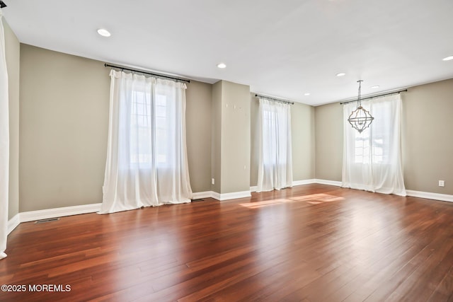 empty room featuring dark wood-type flooring and an inviting chandelier