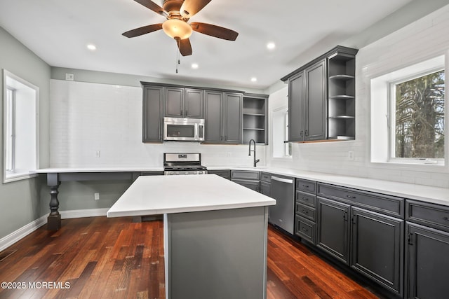 kitchen featuring stainless steel appliances, sink, a center island, ceiling fan, and dark wood-type flooring