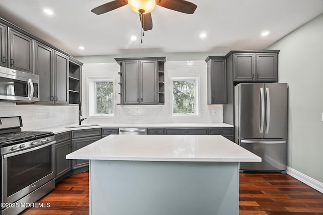 kitchen featuring stainless steel appliances, a kitchen island, gray cabinets, dark hardwood / wood-style flooring, and ceiling fan