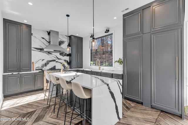 kitchen with island range hood, an island with sink, gray cabinets, parquet floors, and pendant lighting