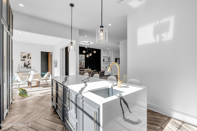 kitchen featuring a kitchen island with sink, light parquet flooring, light stone countertops, pendant lighting, and sink