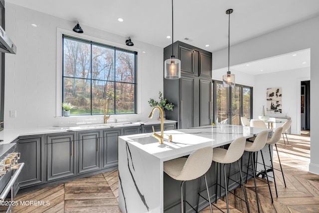 kitchen with light parquet floors, a kitchen island with sink, a kitchen breakfast bar, hanging light fixtures, and high end range