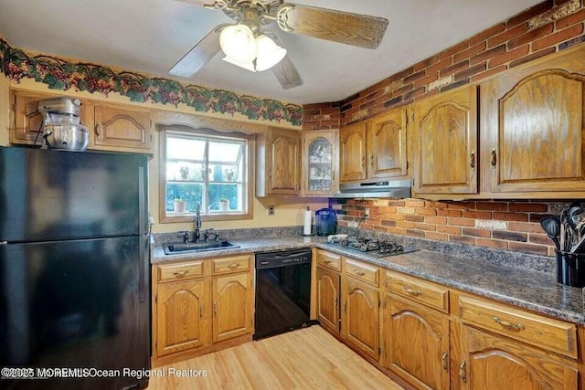 kitchen featuring brick wall, light hardwood / wood-style floors, black appliances, dark stone countertops, and sink