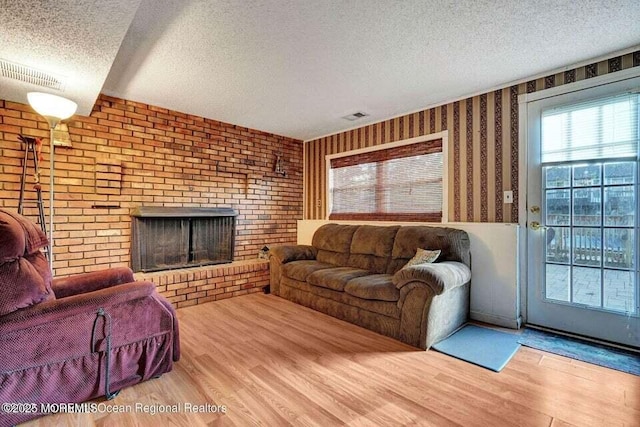 living room featuring a textured ceiling, a brick fireplace, and hardwood / wood-style floors