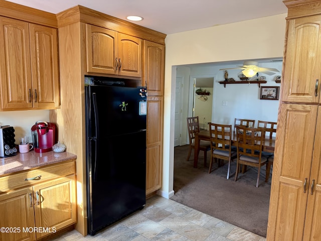 kitchen with ceiling fan, light colored carpet, black refrigerator, and light stone countertops