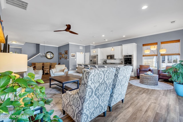 living room featuring ceiling fan, light wood-type flooring, and ornamental molding