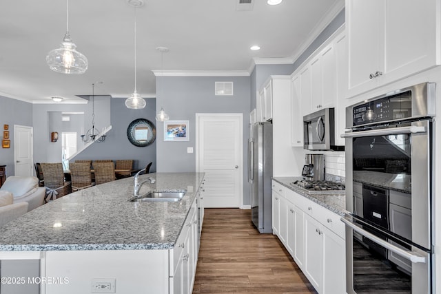 kitchen featuring stainless steel appliances, white cabinets, a kitchen island with sink, and hanging light fixtures