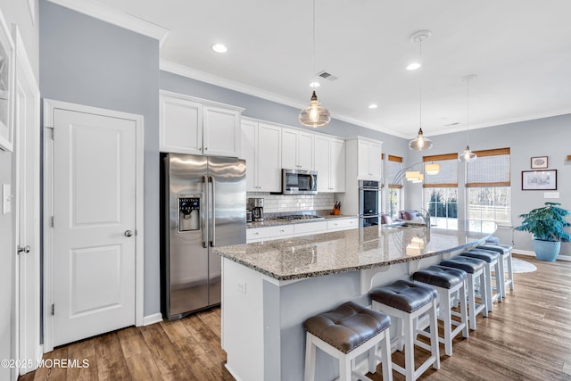 kitchen featuring a kitchen island with sink, appliances with stainless steel finishes, hanging light fixtures, a breakfast bar, and white cabinetry